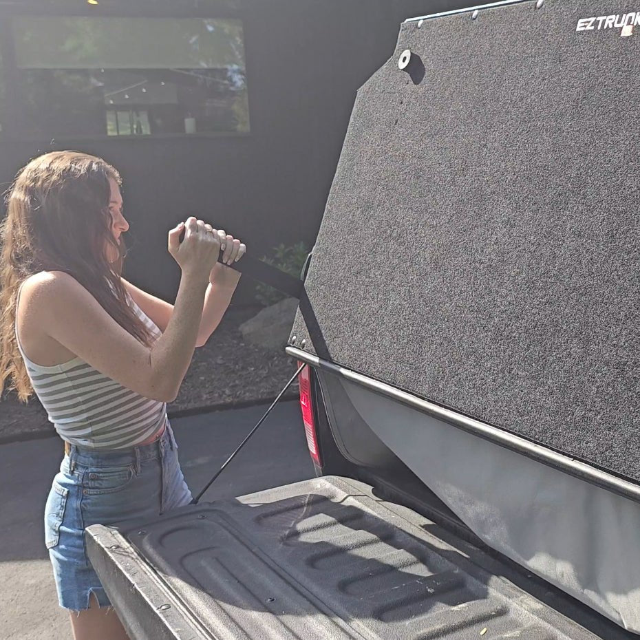 Woman using handle to convert black EZ Trunk from a truck bed extender into secure cargo storage space inside the truck bed.