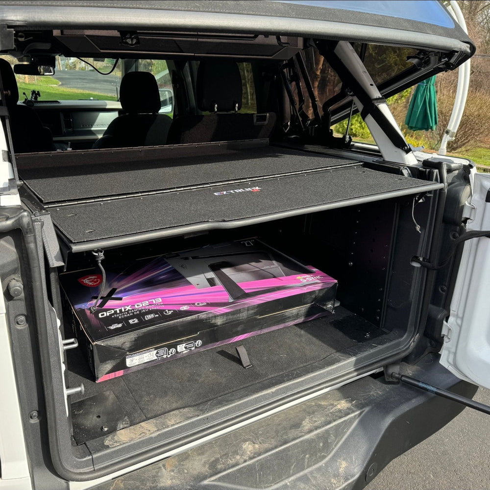 Folding security trunk installed in the cargo area of a Jeep JKU 4 Door vehicle, with a black carpeted interior.