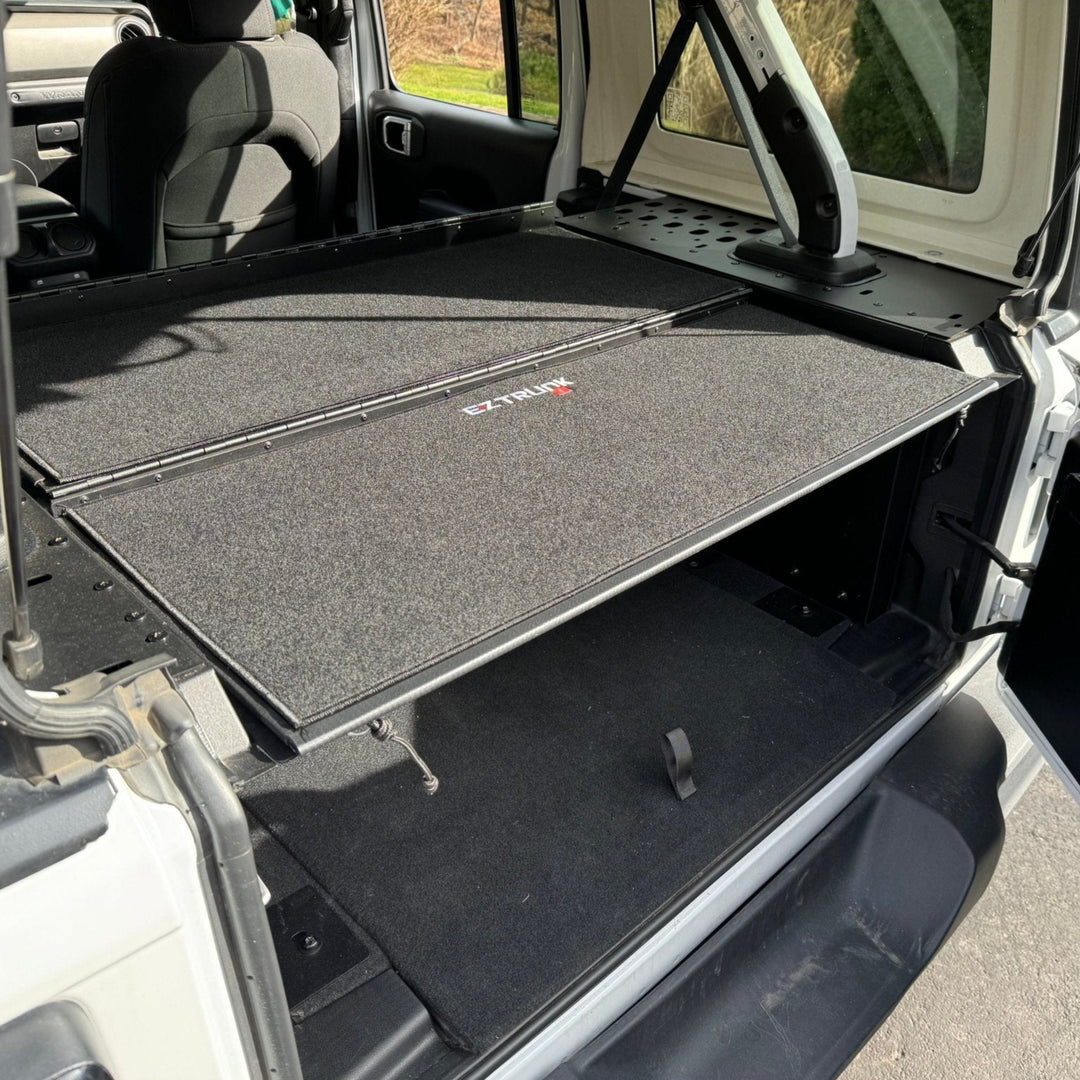 Folding security trunk installed in the cargo area of a Jeep JKU 4 Door vehicle, with a black carpeted interior.