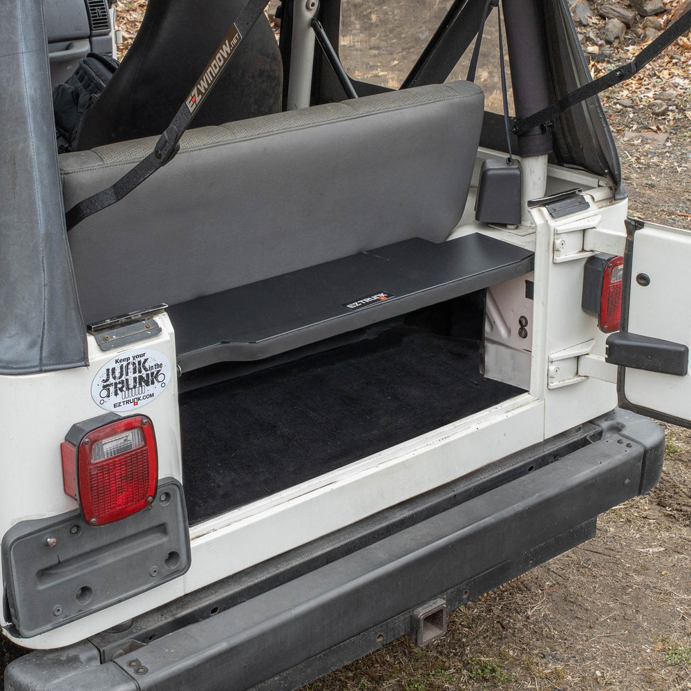 Black EZTrunk installed in cargo area of white Jeep TJ Wrangler with trunk door open, showing secure storage setup.