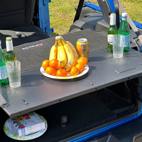 EZTrunk Tailgate Extension Table open in Jeep with fruit and drinks on top, plates and napkins stored on shelf below.