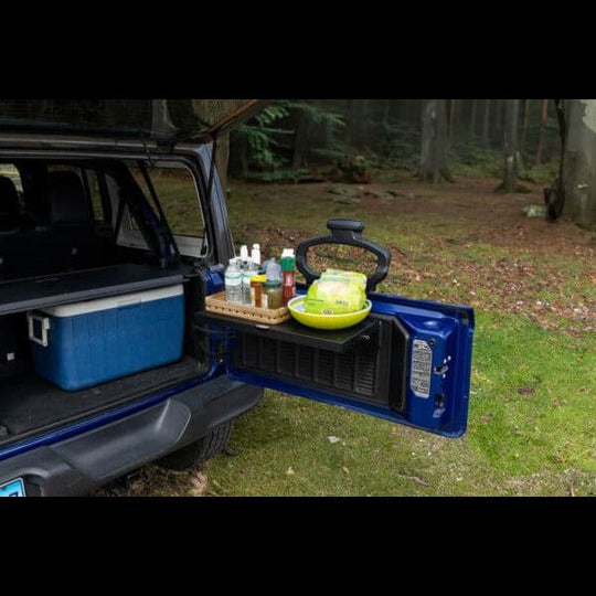 Aftermarket black foldable tailgate table mounted on Jeep, shown holding food and drinks—perfect for camping and tailgating.