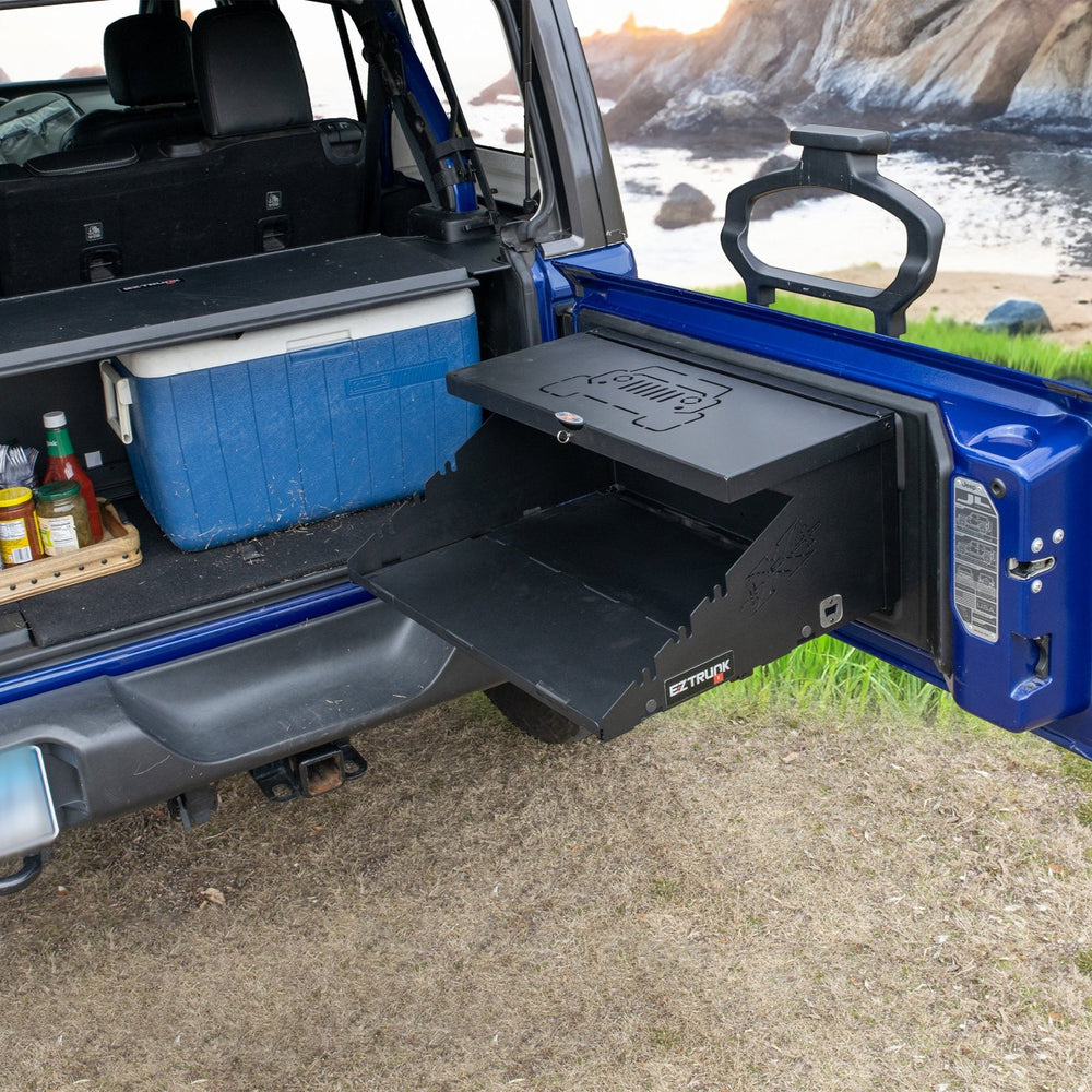 Empty Extreme Folding Tailgate in blue Jeep, with condiments and cooler stored in the back for outdoor use.