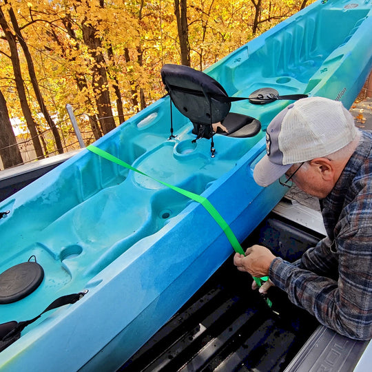 Man securing blue kayak in truck bed with Truck Buddiez straps, showcasing heavy-duty, adjustable, and reliable cargo safety.