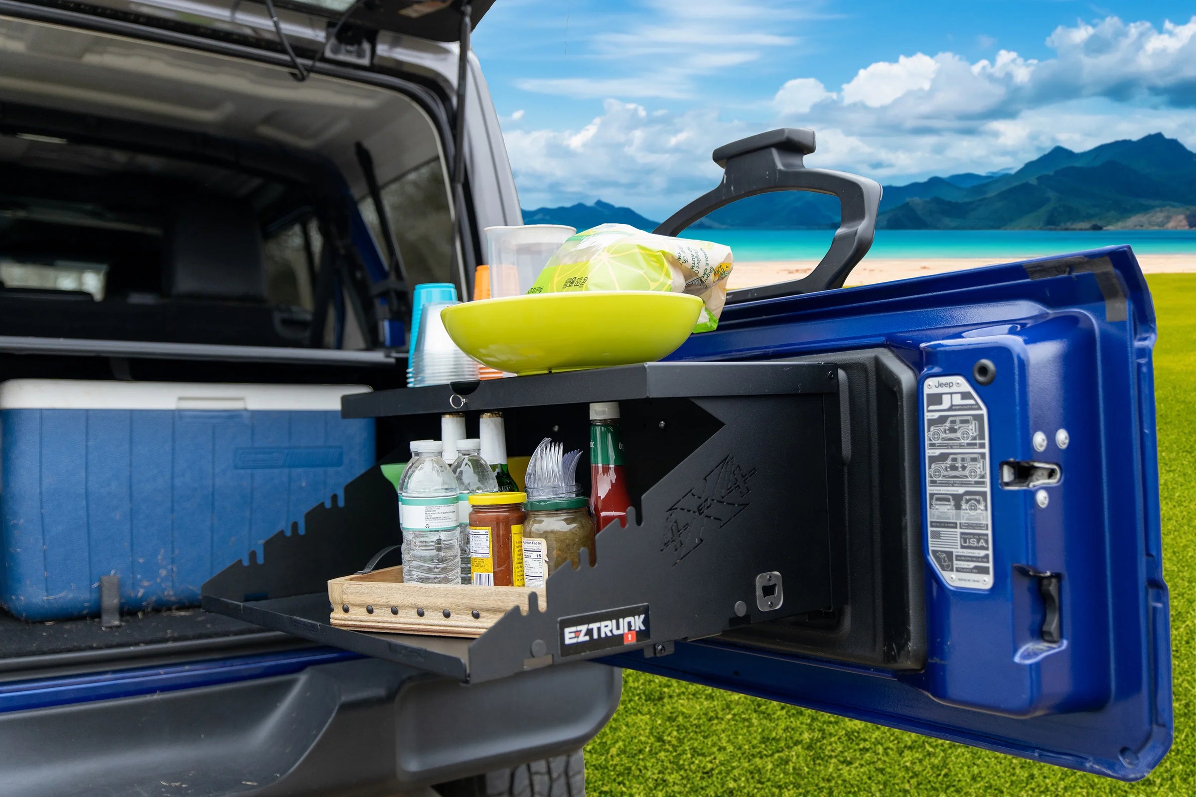 Extreme Tailgate Table by EZ4X4 installed on blue Jeep tailgate, neatly storing food and drinks for outdoor use.