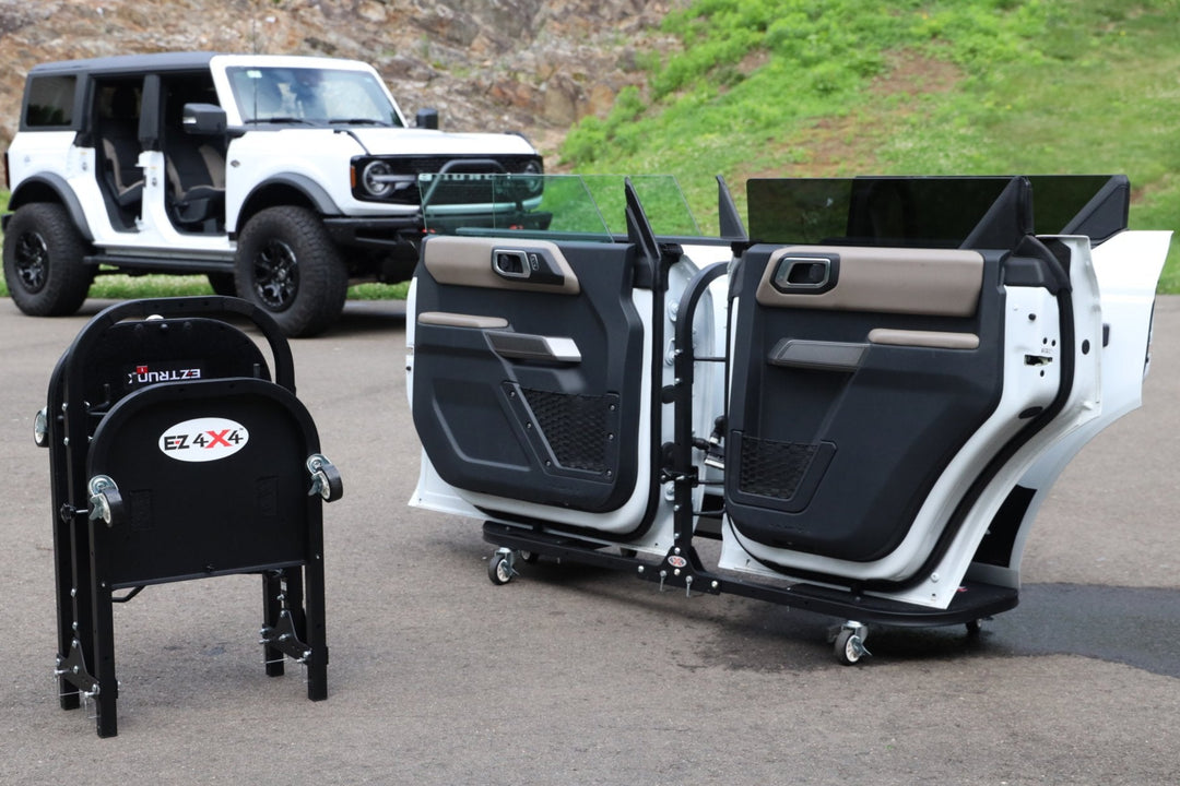 White Ford Bronco with doors stored on EZ4X4 door carts; second cart folded for compact, easy transport on driveway.