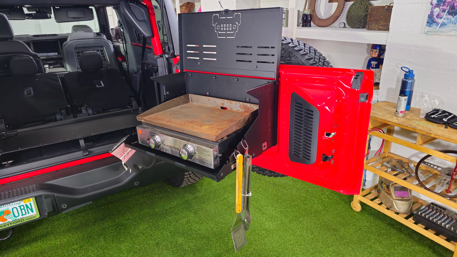EZ4X4 Extreme Tailgate Table on a red Ford Bronco supporting a Blackstone griddle with cooking tongs and a spatula hanging from the built-in hooks.