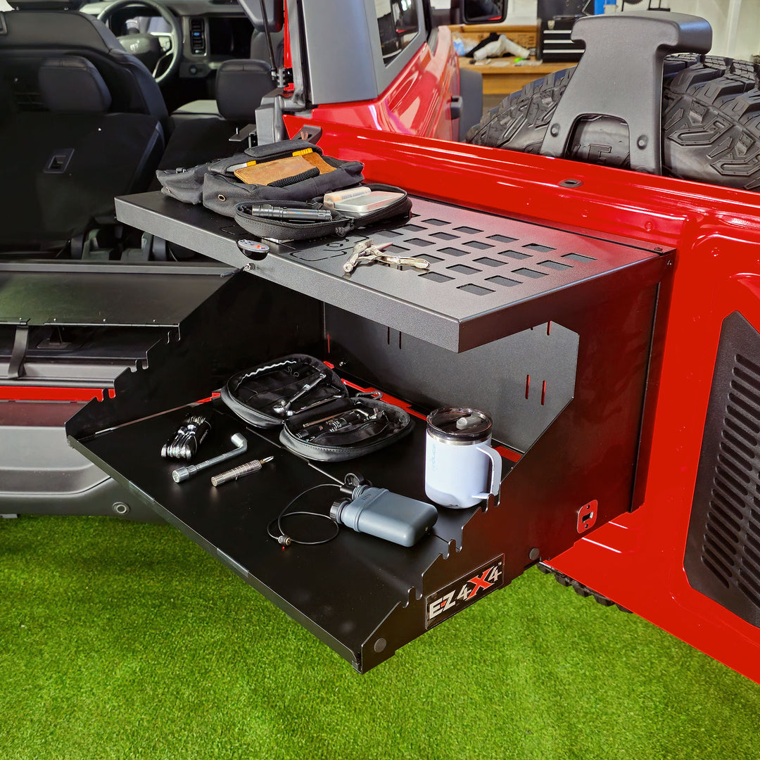 The EZ4X4 Extreme Bronco Tailgate Table fully opened, securely supporting gear on its main surface and utilizing the integrated MOLLE panel for additional storage.