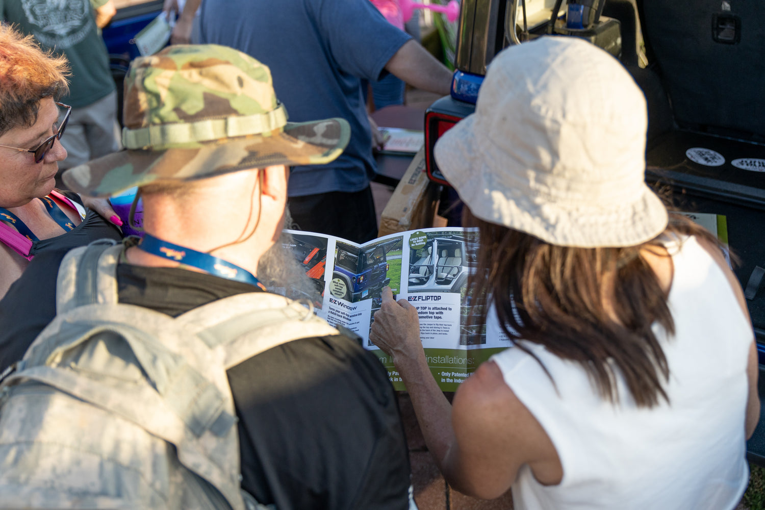 Woman pointing out a product in an EZ4X4 brochure while two other people look on at an outdoor event.