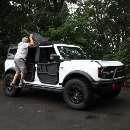 Person opening Ford Bronco EZ Flip-Top panels, showing ease of use and off-road convenience of the aftermarket roof system.