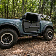 Blue 2-door Ford Bronco fitted with EZ4X4 Alpha Tube Doors and All-Weather Panels set parked on a wooded trail.