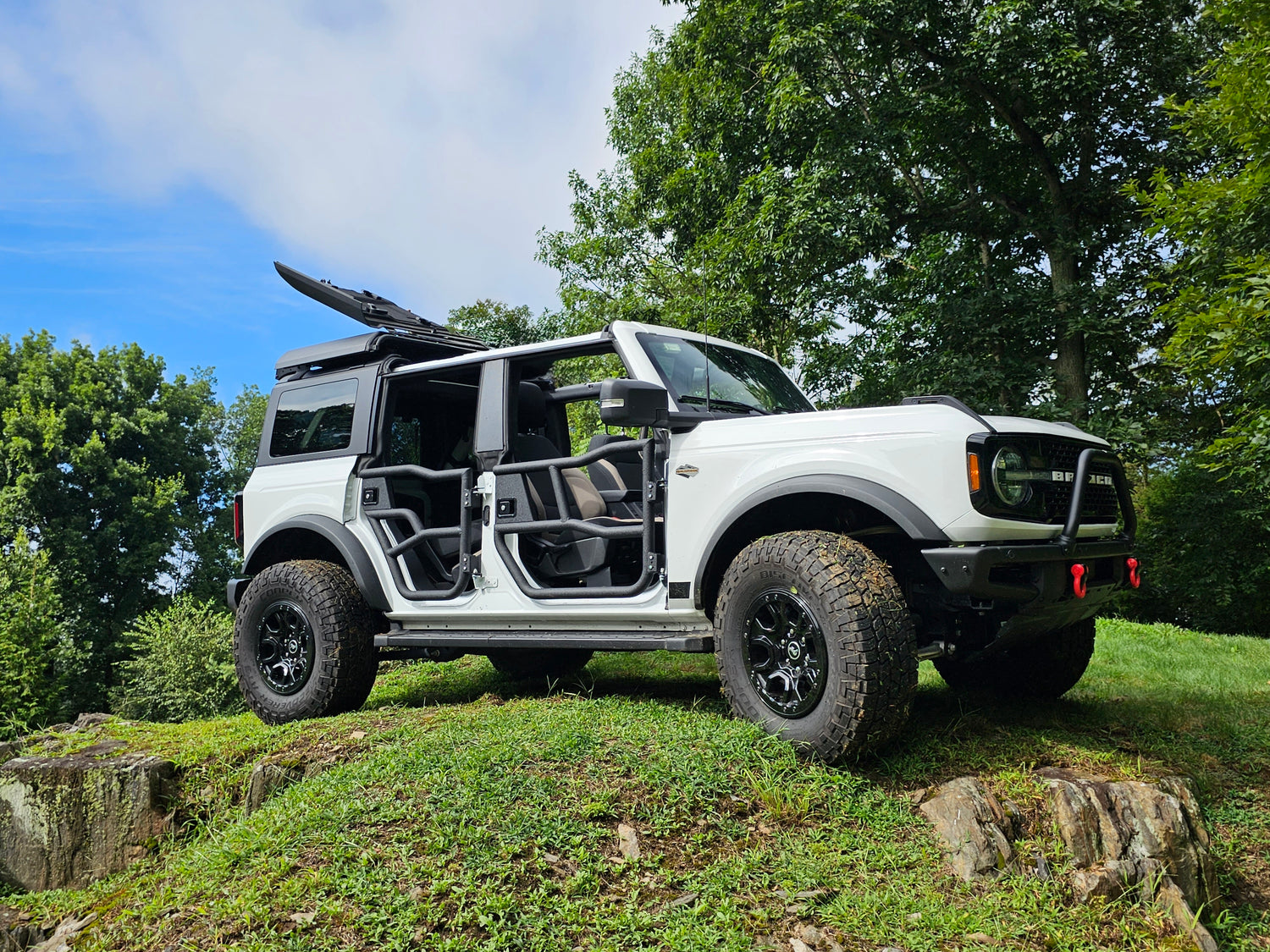 White Ford Bronco equipped with EZ4X4 Alpha Tube Doors, EZ FlipTop, and Middle Panel Roof Rack Holder parked on a grassy hillside.