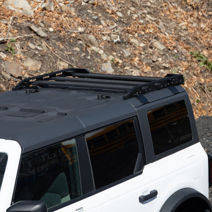 White Ford Bronco with roof rack system parked in rocky setting, highlighting rugged, outdoor adventure readiness.