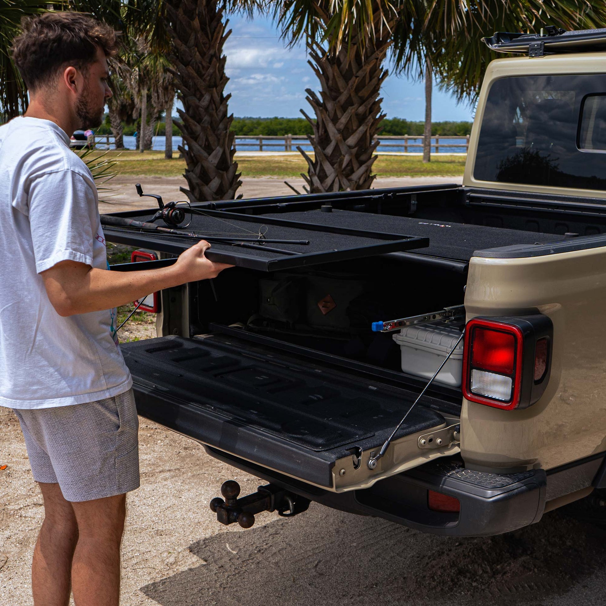 Man inserting pull-out shelf for EZTrunk in Jeep Gladiator truck bed, showcasing modular storage and easy cargo access.