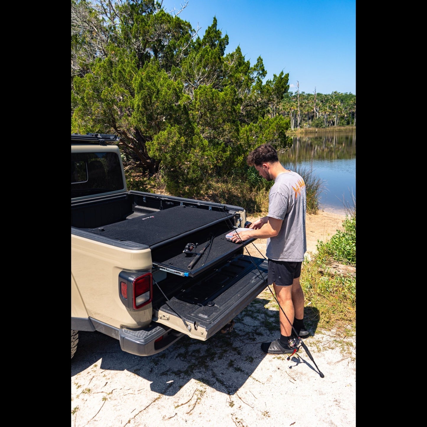 Man using sliding top shelf in Jeep Gladiator trunk outdoors, showing easy cargo access and organized off-road storage.