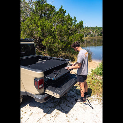 Man using sliding top shelf in Jeep Gladiator trunk outdoors, showing easy cargo access and organized off-road storage.