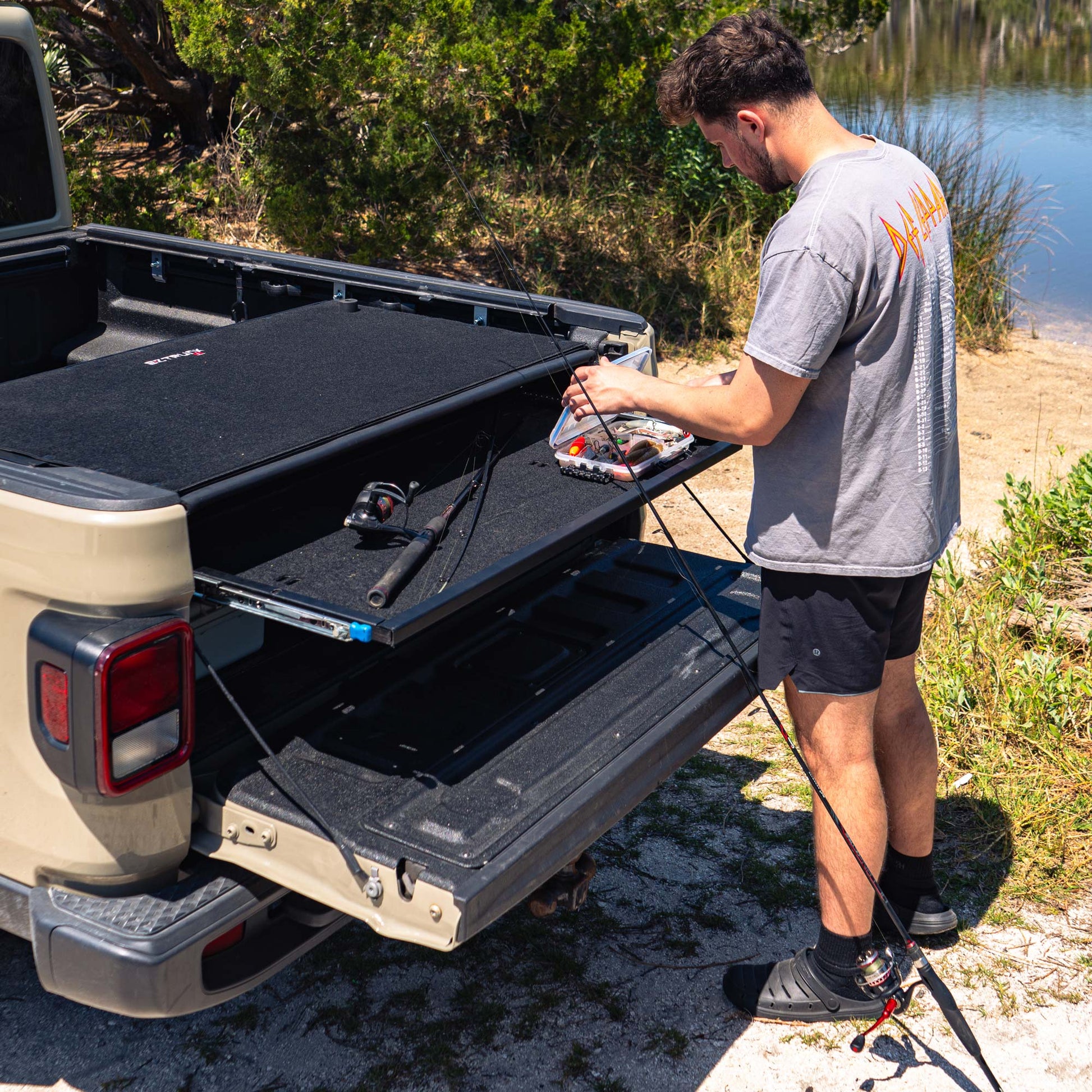 Man using EZTrunk pull-out shelf in Jeep Gladiator to prep fishing gear, highlighting organized, modular truck bed storage.