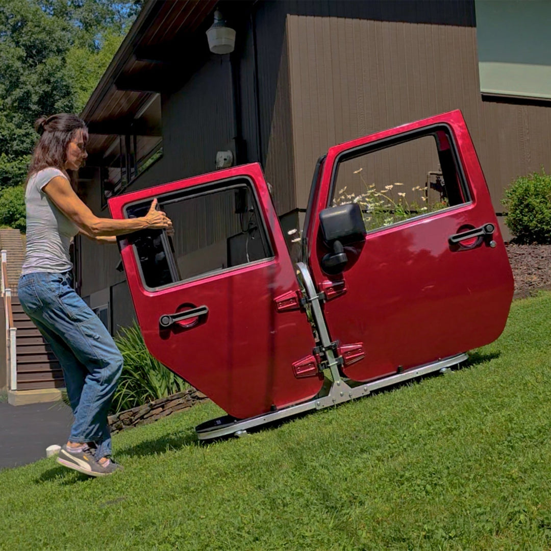 Woman rolling four red Jeep doors down a grassy hill using the EZ4X4 Door Storage Cart.