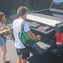 Two people organizing gear with a shelf inside the black EZ Trunk, showcasing versatile cargo storage and space optimization.