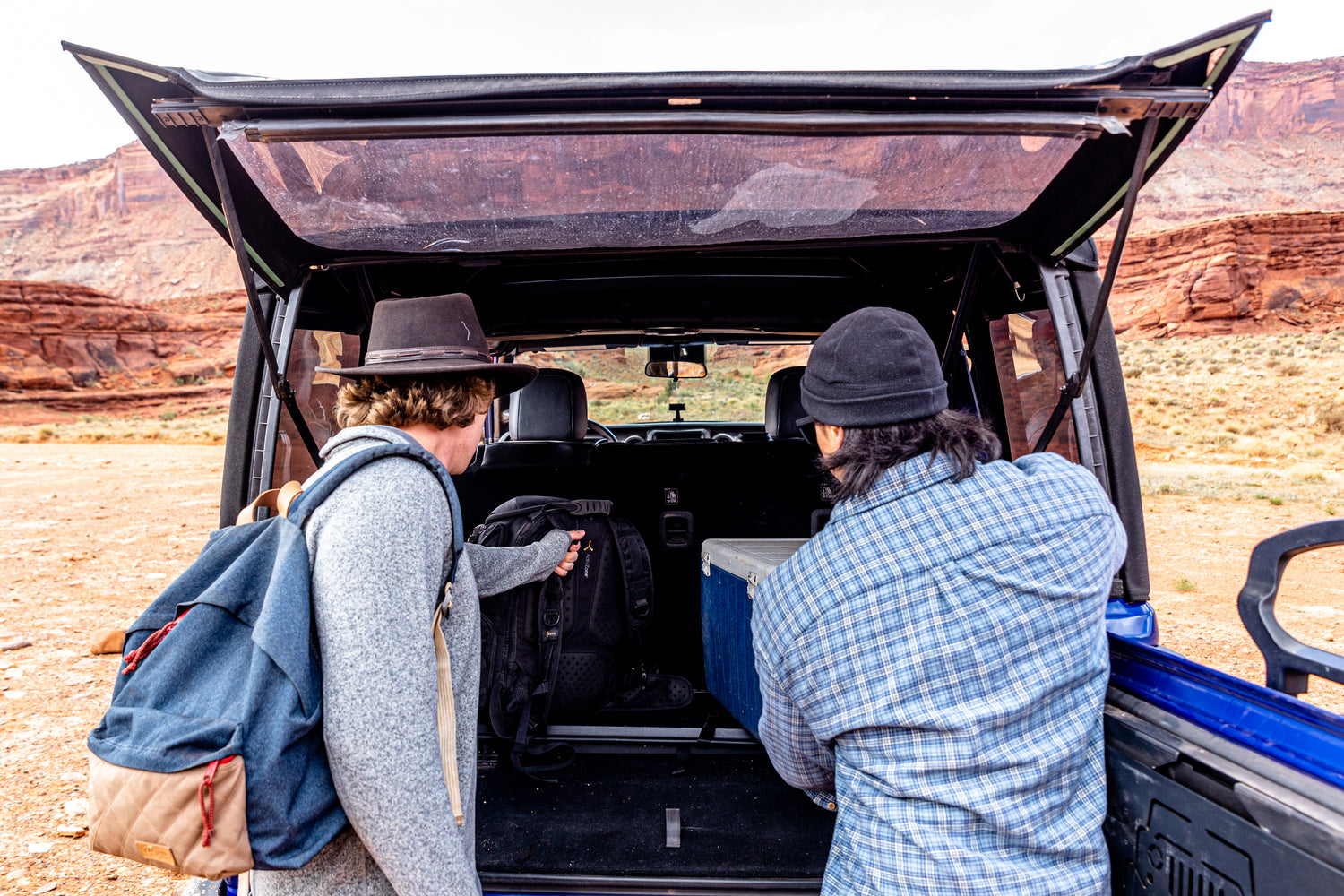 EZ4X4 EZWindow holding rear Jeep Wrangler window open while two men access cargo in a desert setting.