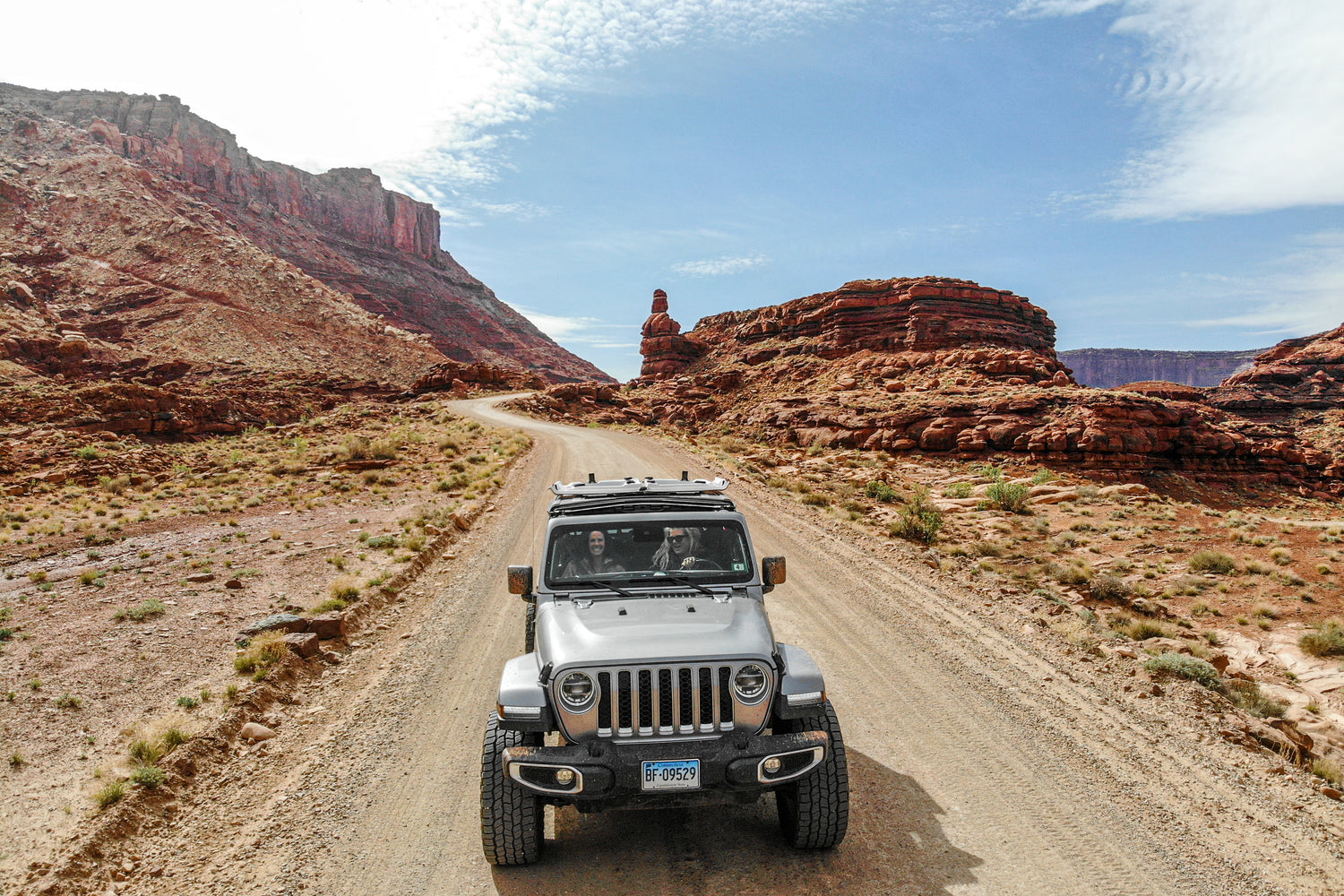 Woman driving a silver Jeep Wrangler on a desert dirt road with Freedom Panels secured back using the EZ4X4 EZ FlipTop.