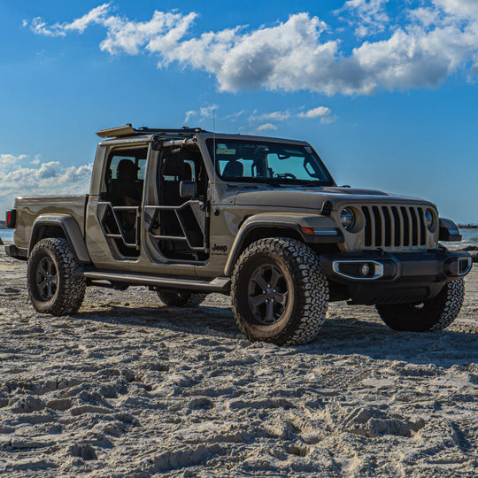 Tan Jeep Gladiator parked on a sandy beach featuring black EZ4X4 Razor Tube Doors and the EZ FlipTop securing the open freedom panels.