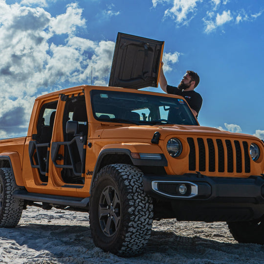 Yellow Jeep Gladiator (JT) on a sandy beach, with a man flipping back and securing the Freedom Panels using the EZ4X4 EZ FlipTop system.