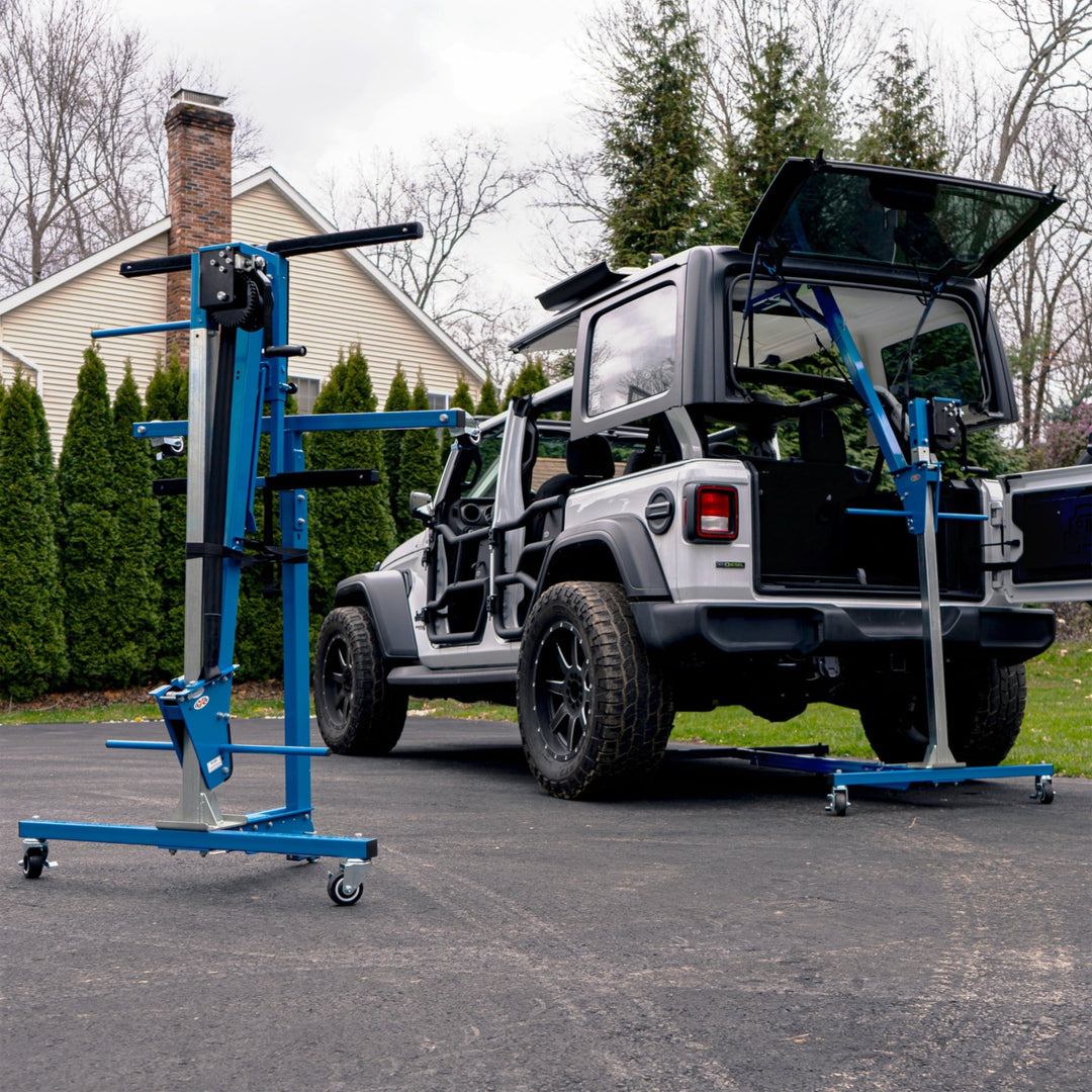 White Jeep Wrangler on a driveway equipped with EZ4X4 Alpha Tube Doors and mirrors, with the Hard Top Remover Lift storing the roof overhead and a second folded lift nearby.