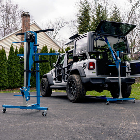 White Jeep Wrangler on a driveway equipped with EZ4X4 Alpha Tube Doors and mirrors, with the Hard Top Remover Lift storing the roof overhead and a second folded lift nearby.