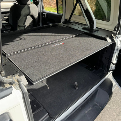 Folding security trunk installed in the cargo area of a Jeep JKU 4 Door vehicle, with a black carpeted interior.