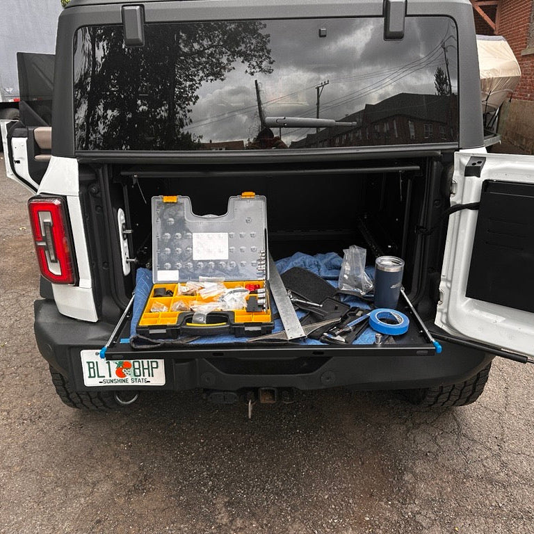 Frontal view of a white Ford Bronco with the EZ4X4 Extreme EZTRUNK shelf fully extended from the back, actively supporting tools and demonstrating its use as a portable work table.