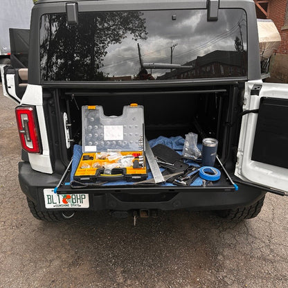 Frontal view of a white Ford Bronco with the EZ4X4 Extreme EZTRUNK shelf fully extended from the back, actively supporting tools and demonstrating its use as a portable work table.