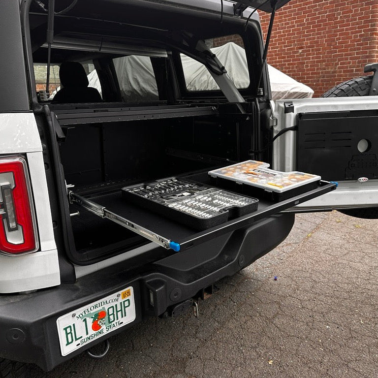Angled view of white Ford Bronco with the EZ4X4 Extreme EZTRUNK shelf pulled out, actively supporting tools and acting as a convenient portable work table.