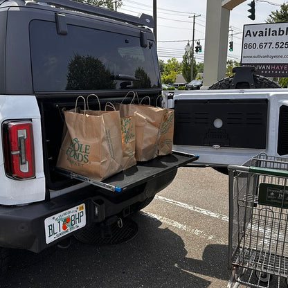 Side view of white Ford Bronco cargo area with EZ4X4 Extreme EZTRUNK and sliding shelf extended holding brown grocery bags.