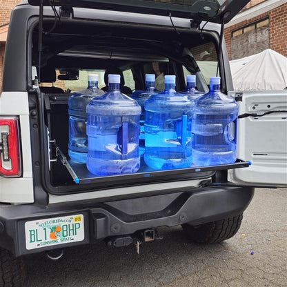 Closer angled view of the extended EZ4X4 Extreme EZTRUNK shelf on a white Ford Bronco supporting six full five-gallon water jugs.