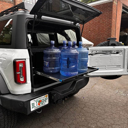 Side view of the extended EZ4X4 Extreme EZTRUNK shelf on a white Ford Bronco supporting five full five-gallon water jugs.