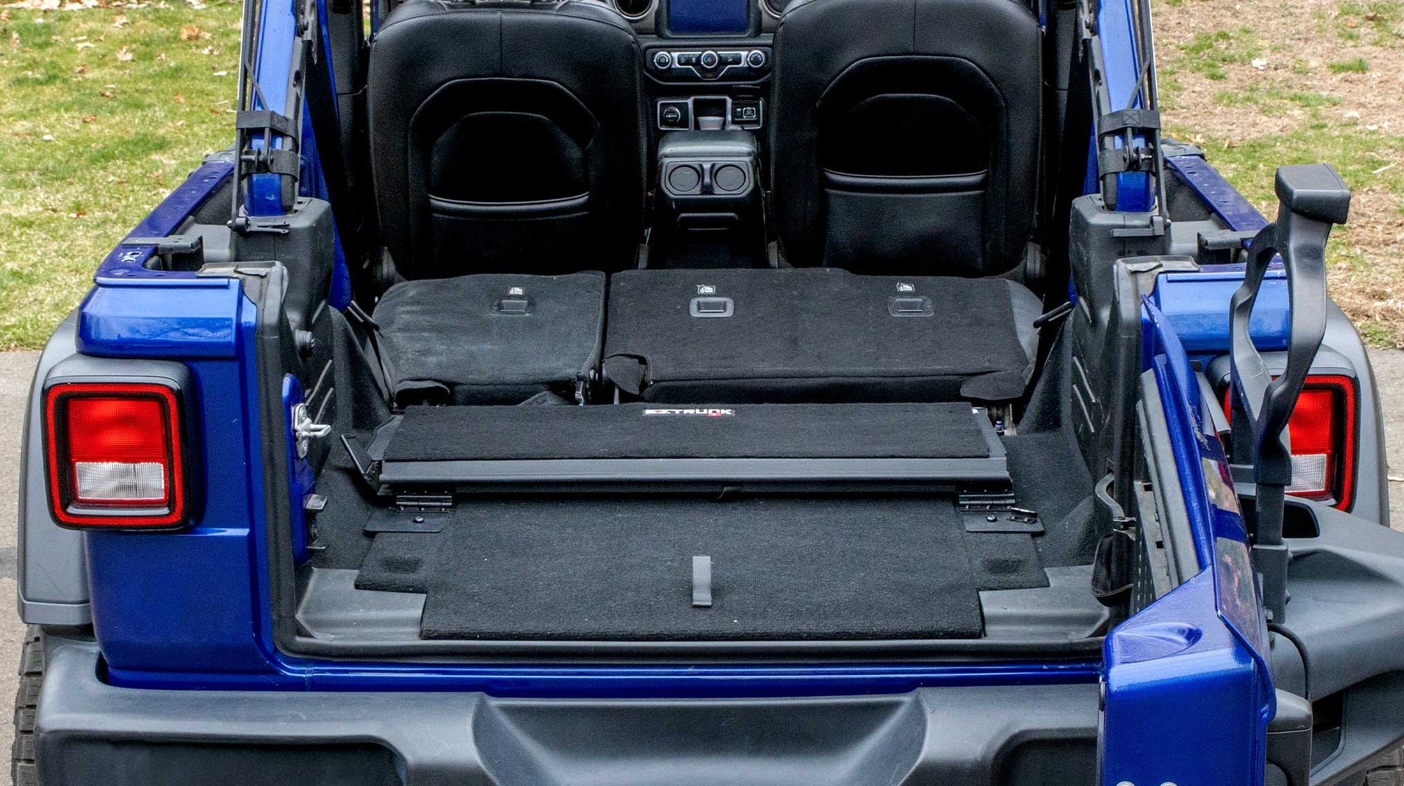 EZ4X4 EZTRUNK installed in a blue Jeep Wrangler, shown fully folded down against the rear cargo area.