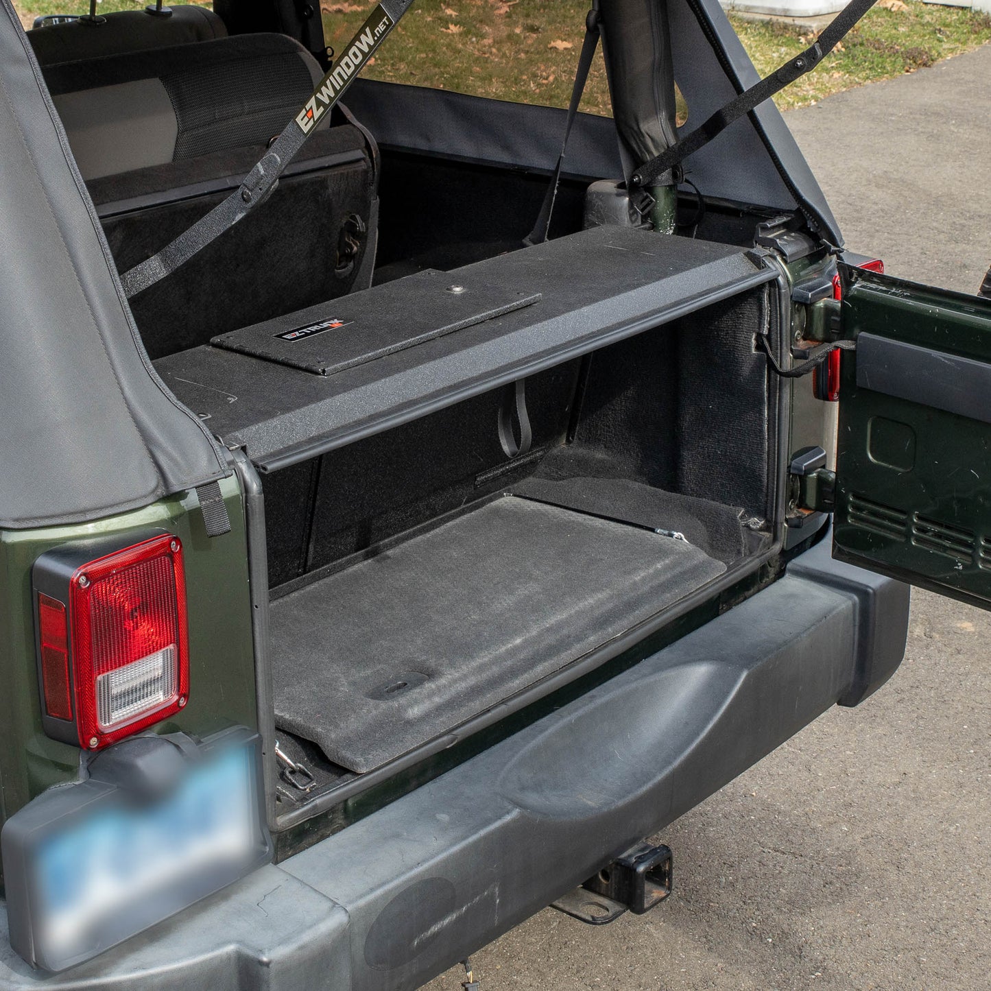 Side view black EZTrunk installed in cargo area of green Jeep Wrangler with trunk door open, showing secure storage setup.