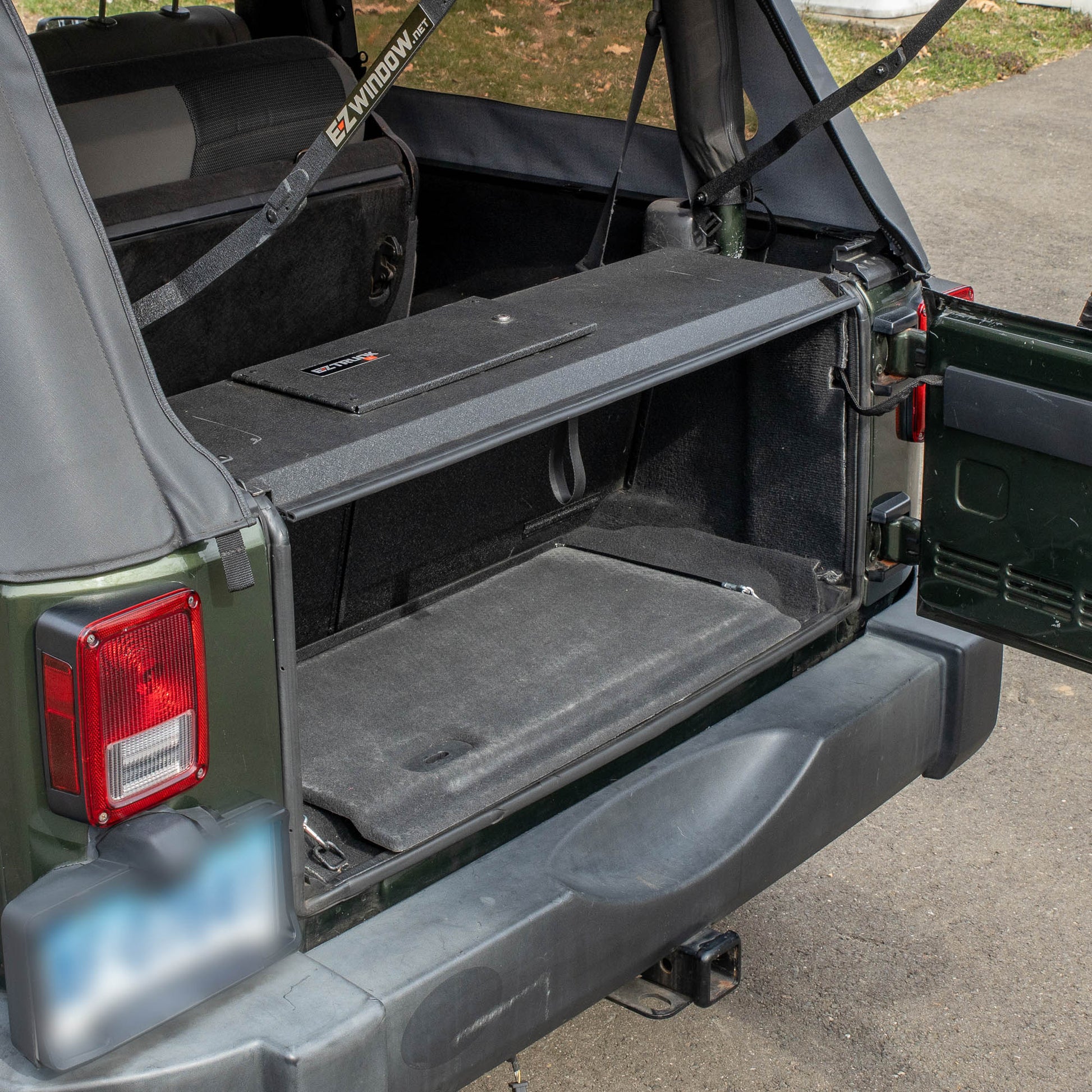 Side view black EZTrunk installed in cargo area of green Jeep Wrangler with trunk door open, showing secure storage setup.