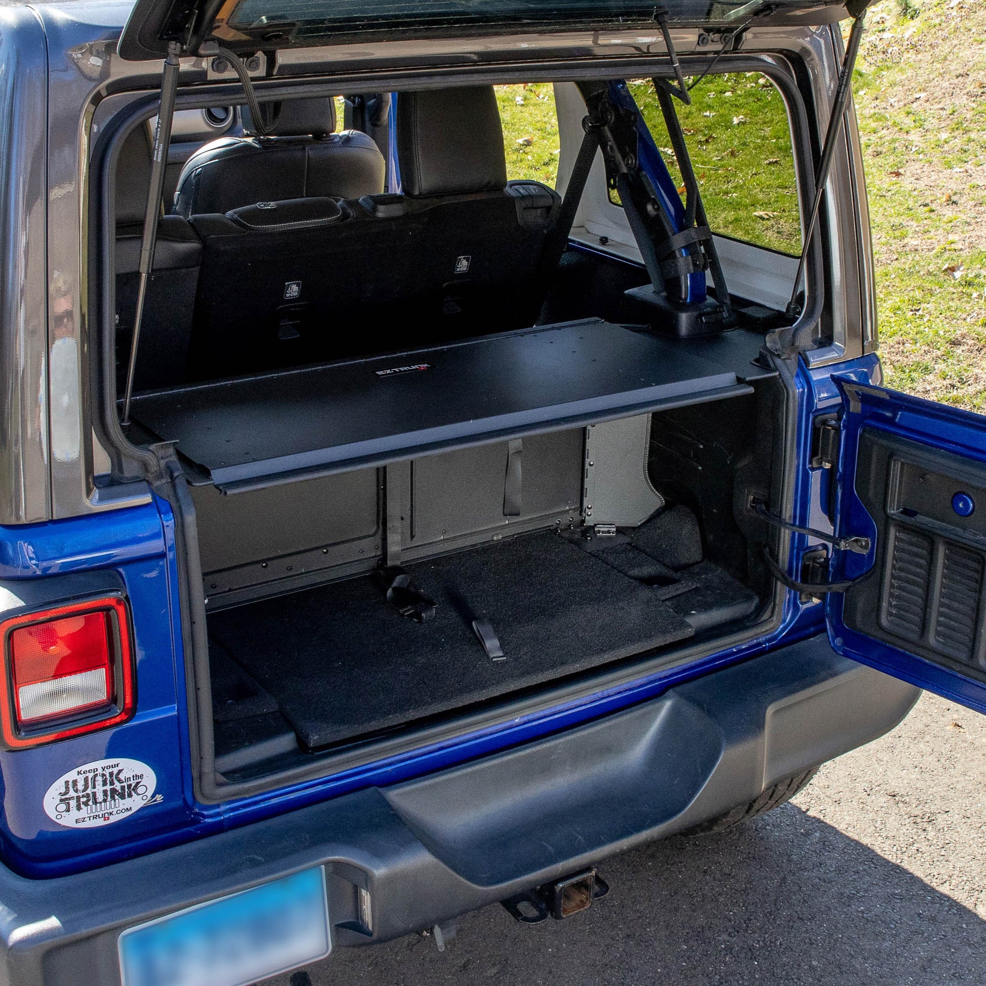 Black EZTrunk installed in blue Jeep Wrangler, shown empty to highlight spacious, secure aftermarket cargo storage solution.
