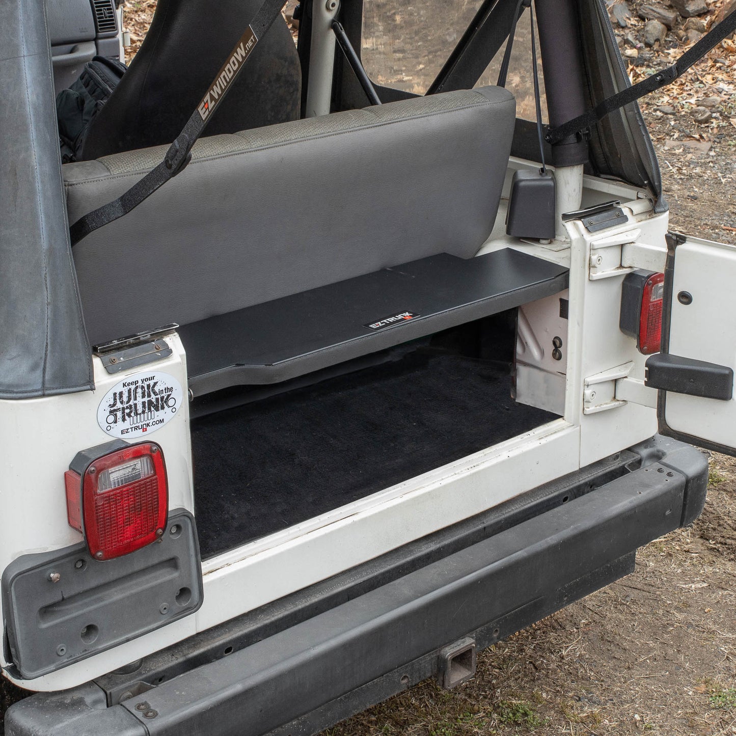 Black EZTrunk installed in cargo area of white Jeep TJ Wrangler with trunk door open, showing secure storage setup.