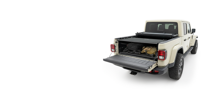 A tan Jeep Gladiator with the tailgate down, revealing gear secured in the truck bed by an EZ4X4 cargo management system under a partially open tonneau cover.