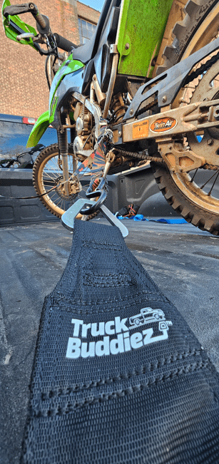 Truck Buddiez straps securing dirt bike in truck bed, providing heavy-duty, adjustable cargo safety for off-road transport.