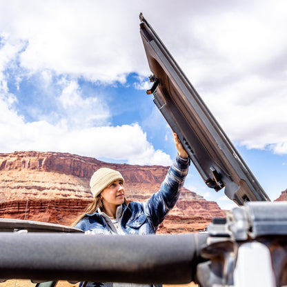 Woman flipping back Freedom Panels of a Jeep outdoors, showing easy roof opening for ventilation and open-air driving.