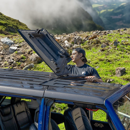 Man flipping back Freedom Panels of a Jeep outdoors, showing easy roof opening for ventilation and open-air driving.