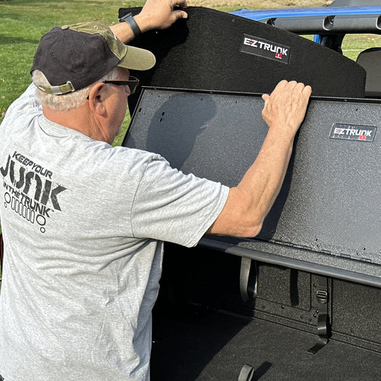 Man installing custom-fit carpet kit in EZ trunk, demonstrating easy install and durable interior protection.