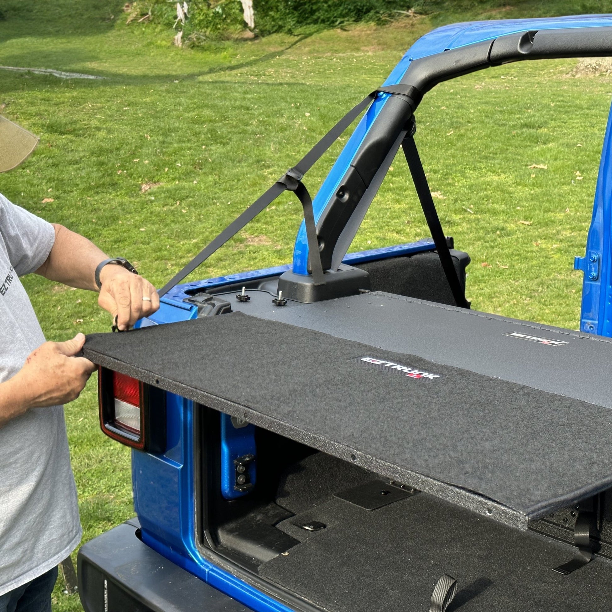 Man demonstrating easy install of custom-fit carpet kit in EZ trunk, showcasing durable interior protection and style.