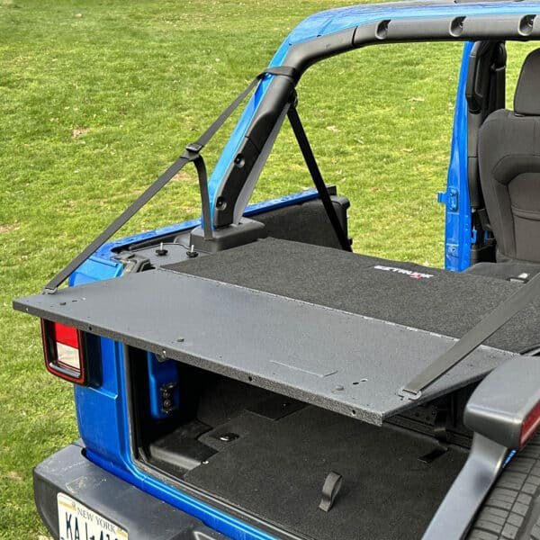 EZ4X4 EZTRUNK Tailgate Extension Table fully extended from blue Jeep Wrangler in grassy outdoor setting.