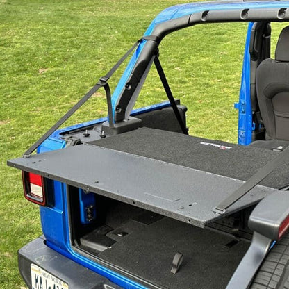 EZ4X4 EZTRUNK Tailgate Extension Table fully extended from blue Jeep Wrangler in grassy outdoor setting.