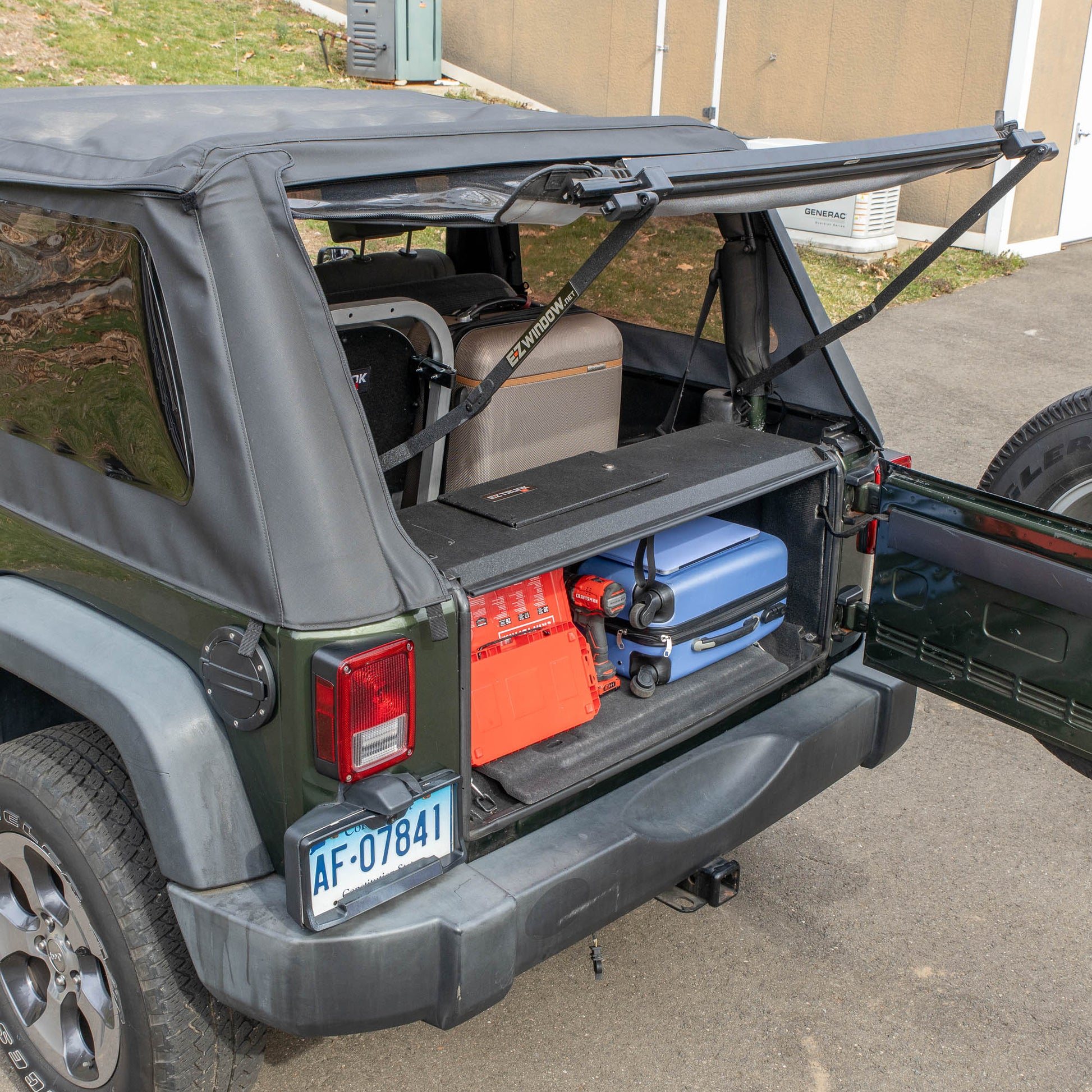 Side view of black EZTrunk installed with items inside cargo area of Jeep Wrangler with trunk door open, showing storage use.